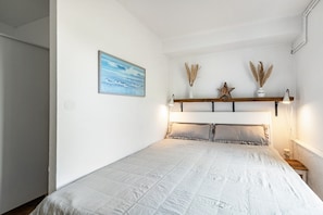 A bedroom with a bed, a nightstand, a wall-mounted shelf with decorative items, and a painting on the wall.