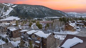 Ett semesterområde med flera trähus, en skidbacke och snötäckta berg i bakgrunden.