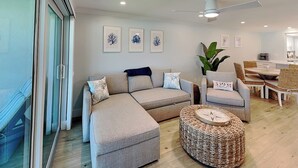 Un salon moderne avec un canapé d’angle, un pouf rond en fibres tressées et un coin repas comprenant une table et des chaises.