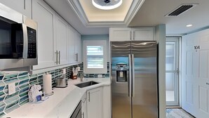Une cuisine moderne avec des meubles blancs, un réfrigérateur en acier inoxydable, un four à micro-ondes et un distributeur d’eau.