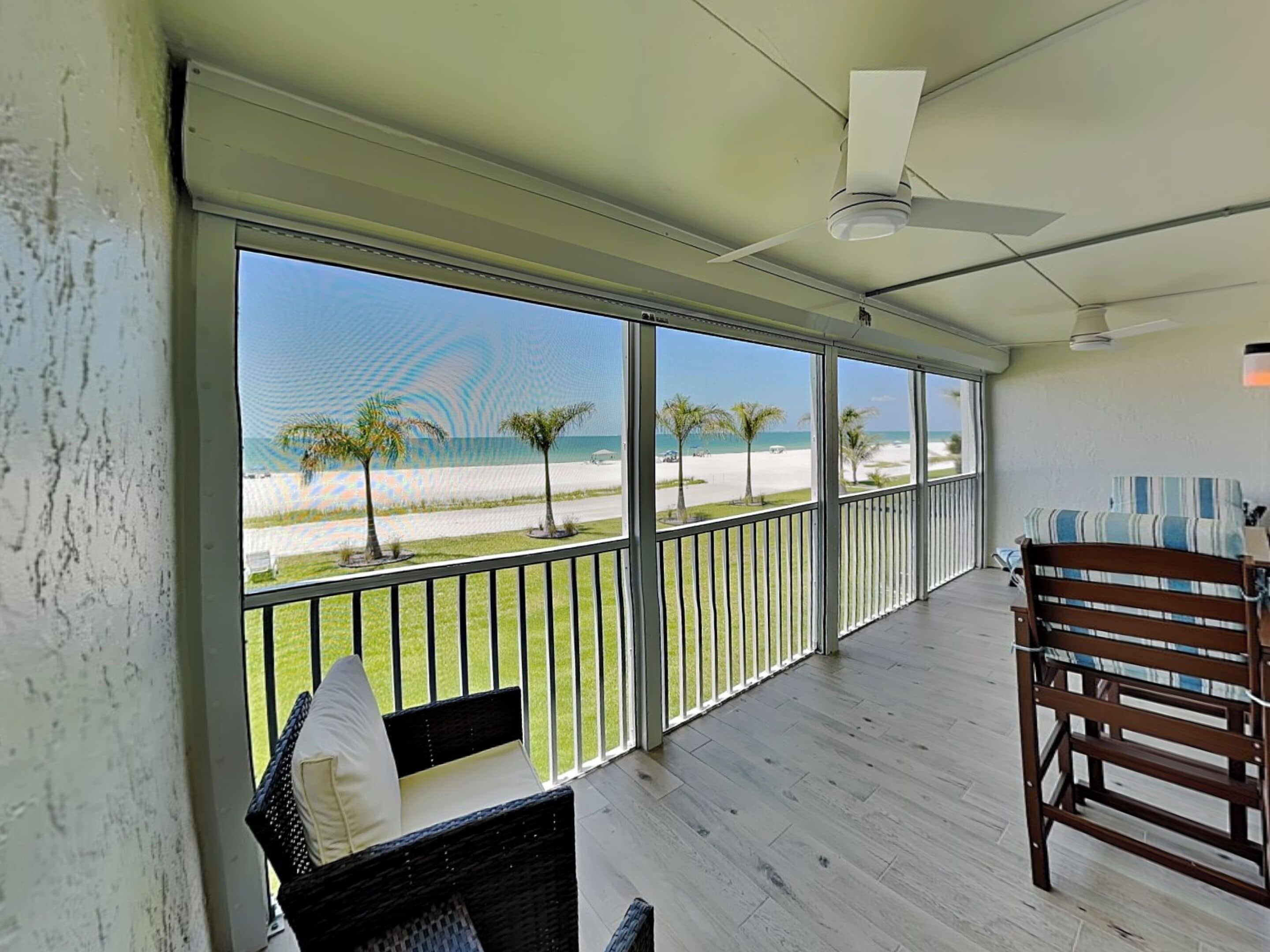 A balcony with a view of the beach, a ceiling fan, and a wicker chair.