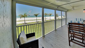 Un balcon avec vue sur la plage, un ventilateur de plafond et un fauteuil en osier.