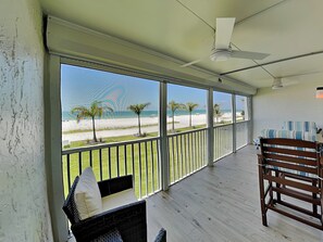 A balcony with a view of the beach, a ceiling fan, and a wicker chair. - Pointe South 104 | Gulf-Front, Screened Lanai, Pool Access + Steps to the Beach (Fort Myers Beach)