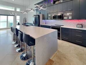 Een moderne keuken met een centraal eiland, barkrukken, roestvrijstalen apparatuur en uitzicht naar buiten.