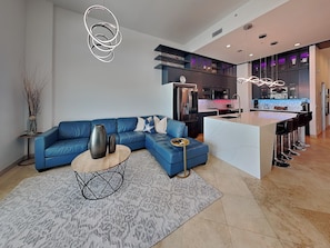 Een moderne woonkamer met een blauwe bank, een salontafel en een keuken met een bar.
