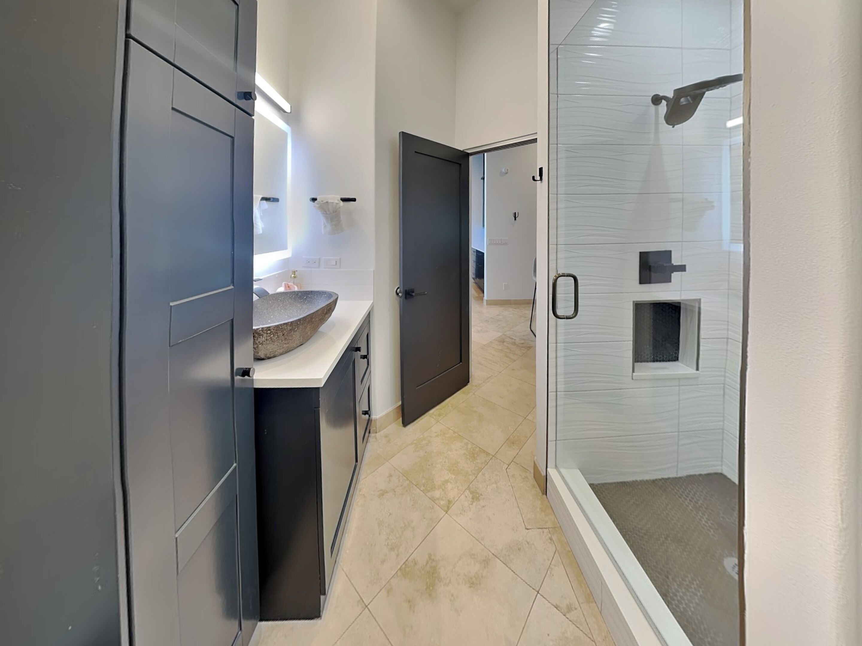 Een moderne badkamer met een groot wastafelmeubel, donkere kastjes en een douchecabine van glas.