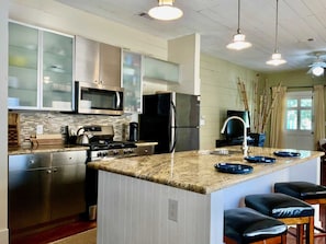 A kitchen with stainless steel appliances, a granite countertop, and a bar area with stools. - Verdant Red Door Retreat (Galveston)