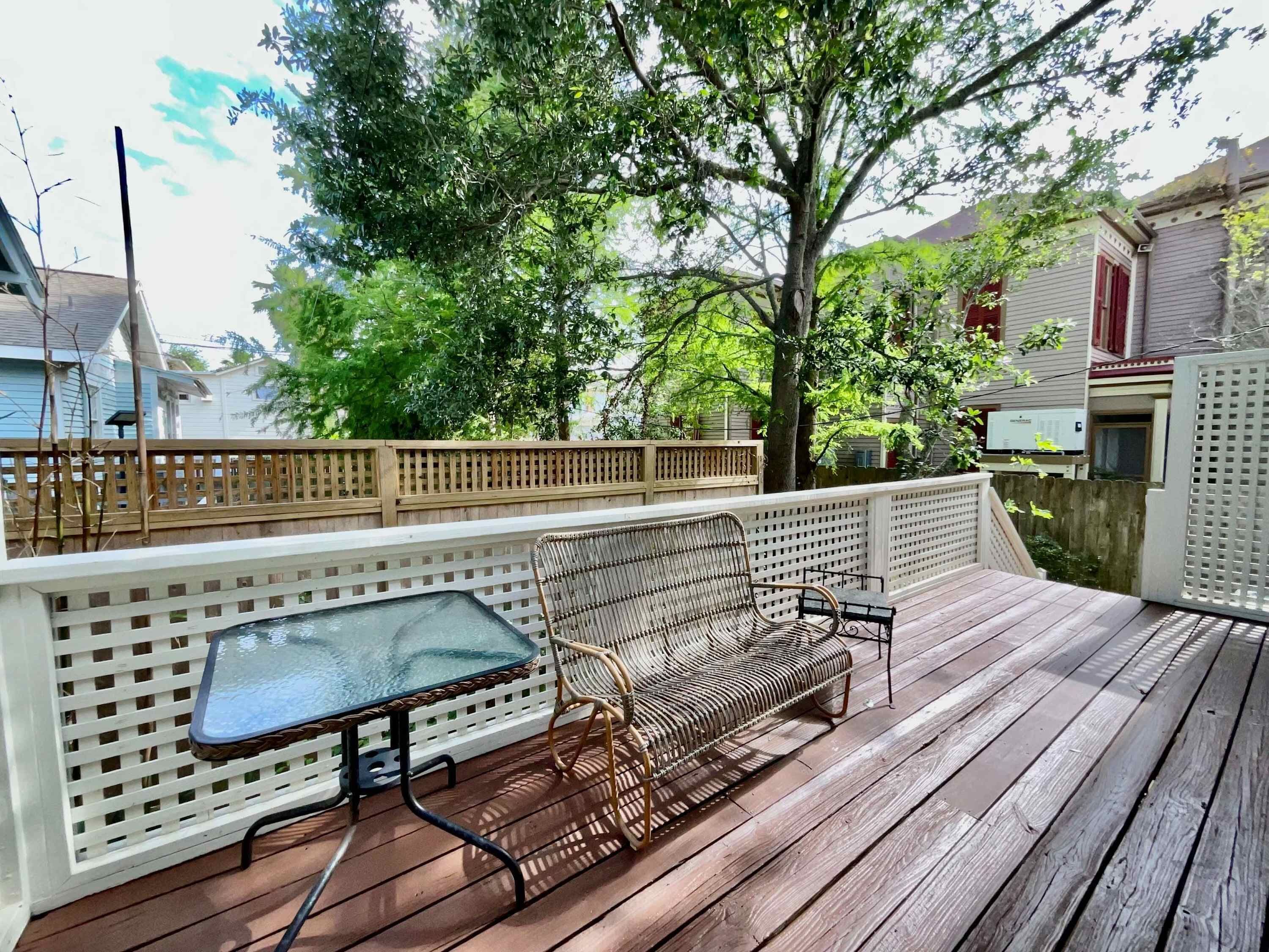 A wooden deck with a glass table and wicker furniture.