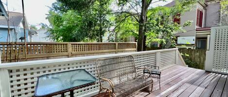 A wooden deck with a glass table and wicker furniture.