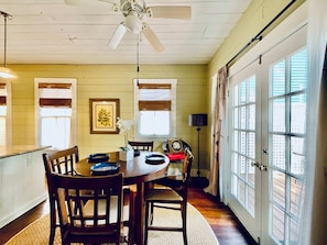 A dining area with a round table, chairs, a ceiling fan, and large windows. - Verdant Red Door Retreat (Galveston)