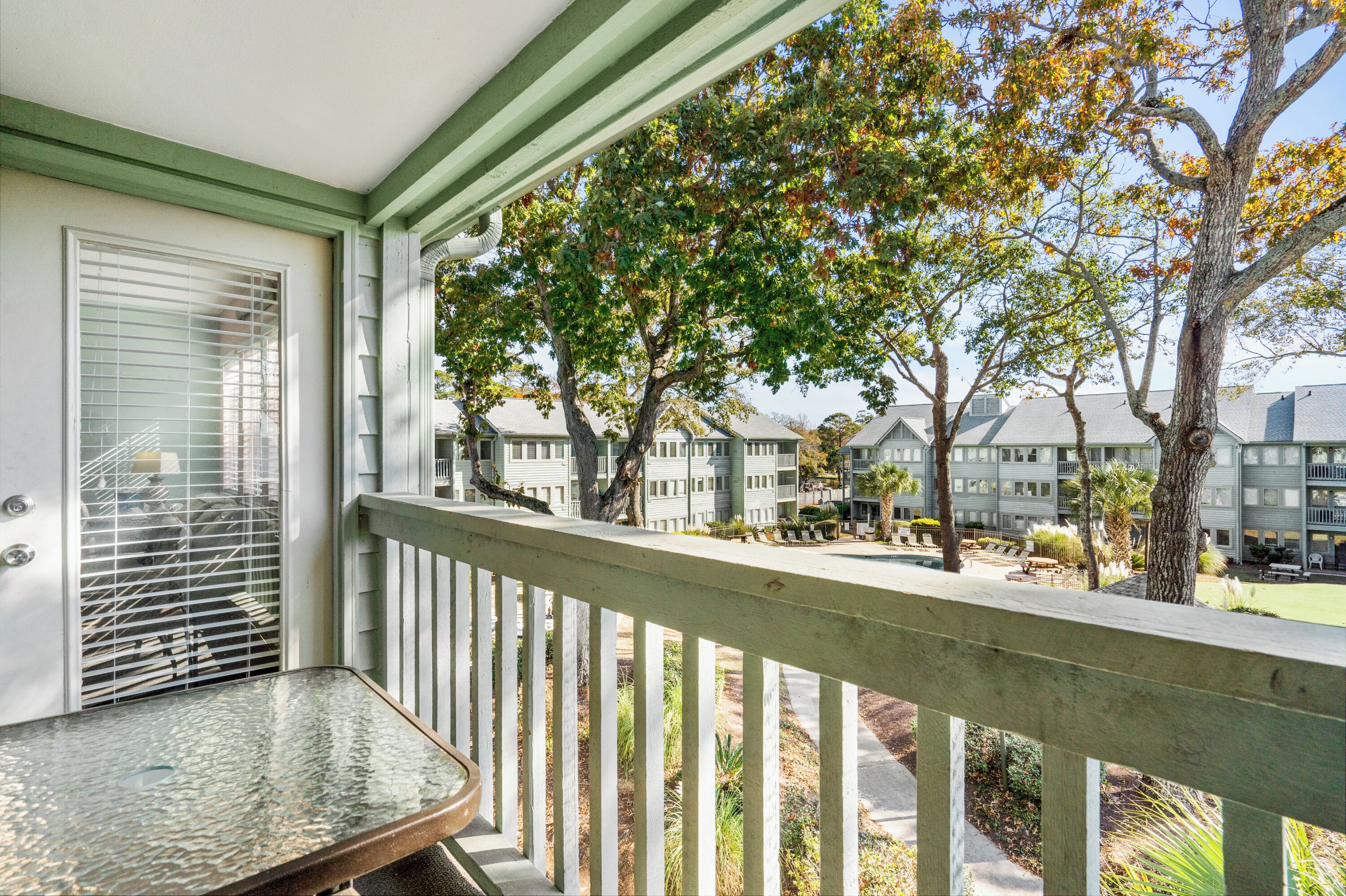A balcony with a table, a view of a building complex, and trees with autumn foliage.