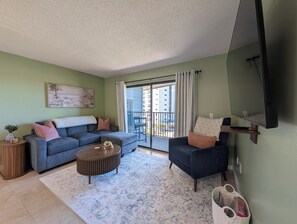 Un salon comprenant un canapé, un fauteuil, une table basse et un téléviseur fixé au mur.