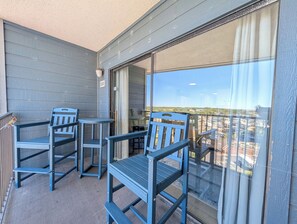 Un balcon avec deux chaises et une table, une porte-fenêtre coulissante et une vue sur le paysage urbain.