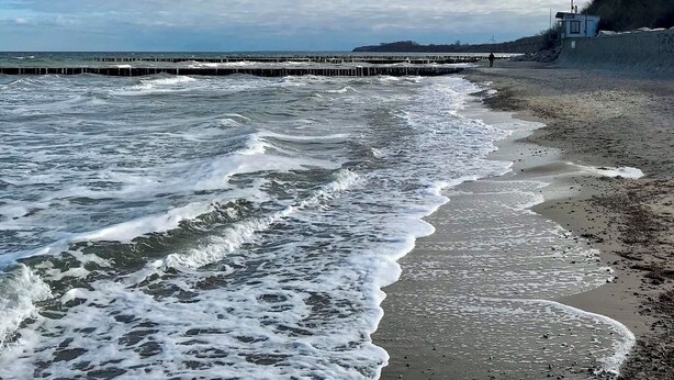 Ein Strand mit Wellen, einem Steg und einem Rettungsturm.