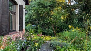 Ein gepflasterter Weg führt zu einem Haus mit Backsteinfassade und Fensterläden.