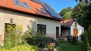 Ein Haus mit roten Ziegeldach, Solaranlage, einem Garten mit verschiedenen Pflanzen und einem Essbereich mit Gartenmöbeln.