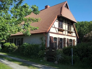 A traditional house with a sloped roof, a visible chimney, and a front porch with a wooden railing. - Cozy 39 m² vacation apartment in the forester's lodge with garden by the forest, near the Baltic Sea (Nienhagen)
