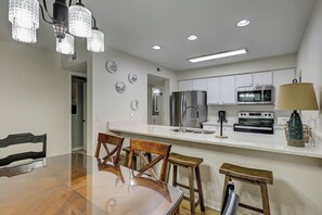 A modern kitchen with stainless steel appliances, a dining area with wooden chairs, and a chandelier. - Sunset Rentals | Moorings 71 | Dog Friendly (Hilton Head Island)