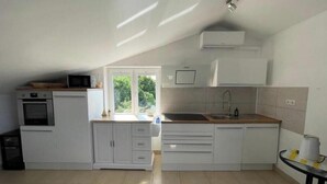 Een keuken met witte kastjes, een ingebouwde oven, een magnetron, een spoelbak en een raam met uitzicht op groen.