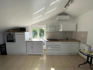A kitchen with white cabinets, a built-in oven, a microwave, a sink, and a window with a view of greenery. - Villa Nordica: Apartamento de 3 dormitorios (Dramalj)