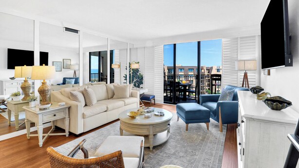 Un salon moderne comprenant un canapé, une table basse et des fauteuils, un coin repas avec une table et des chaises, et une grande fenêtre offrant une vue sur la ville.