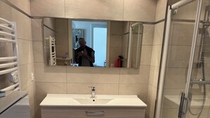 Ett modernt badrum med en stor spegel, ett handfat med två lådor, en duschkabin och ett beige kaklat golv.