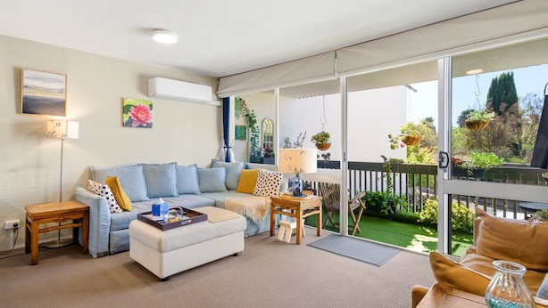 Ein Wohnzimmer mit Sofa, Couchtisch und Blick auf den Garten durch große Fenster.