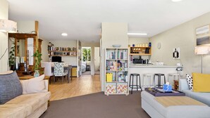 Ein Wohnzimmer mit Sofa, Couchtisch, Bücherregal und einer Küchenzeile mit Arbeitsplatte und Barhocker.