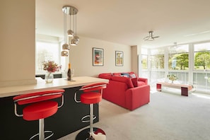 Una cocina moderna con un taburete rojo, un sofá rojo y un ventanal con vistas a árboles.