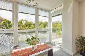 Una habitación con ventanas amplias, una mesa con un florero y una planta en maceta.