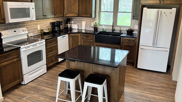 A modern kitchen with wooden cabinets, a central island with stools, a built-in oven, a microwave, a refrigerator, and a window providing natural light.