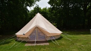 A large, beige, pyramid-shaped tent with a central entrance, set on a grassy field with trees in the background. - TIPI TENT (Callen)