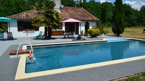 A swimming pool with a tiled deck, a wooden deck chair, a lounge chair, and a small table with a pink umbrella. - TIPI TENT (Callen)
