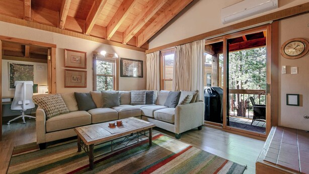 A spacious living room with a large sofa, a coffee table, and a sliding glass door leading to an outdoor area. - The Golden Bend Cozy Stay (Truckee)