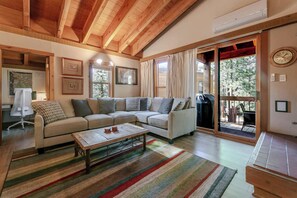A spacious living room with a large sofa, a coffee table, and a sliding glass door leading to an outdoor area. - The Golden Bend Cozy Stay (Truckee)