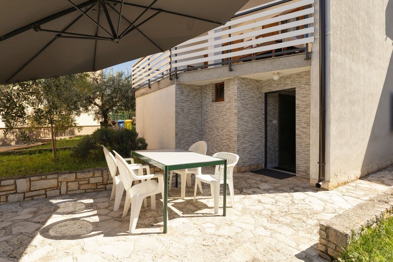 A patio with a table and chairs, a white railing, and a stone wall.