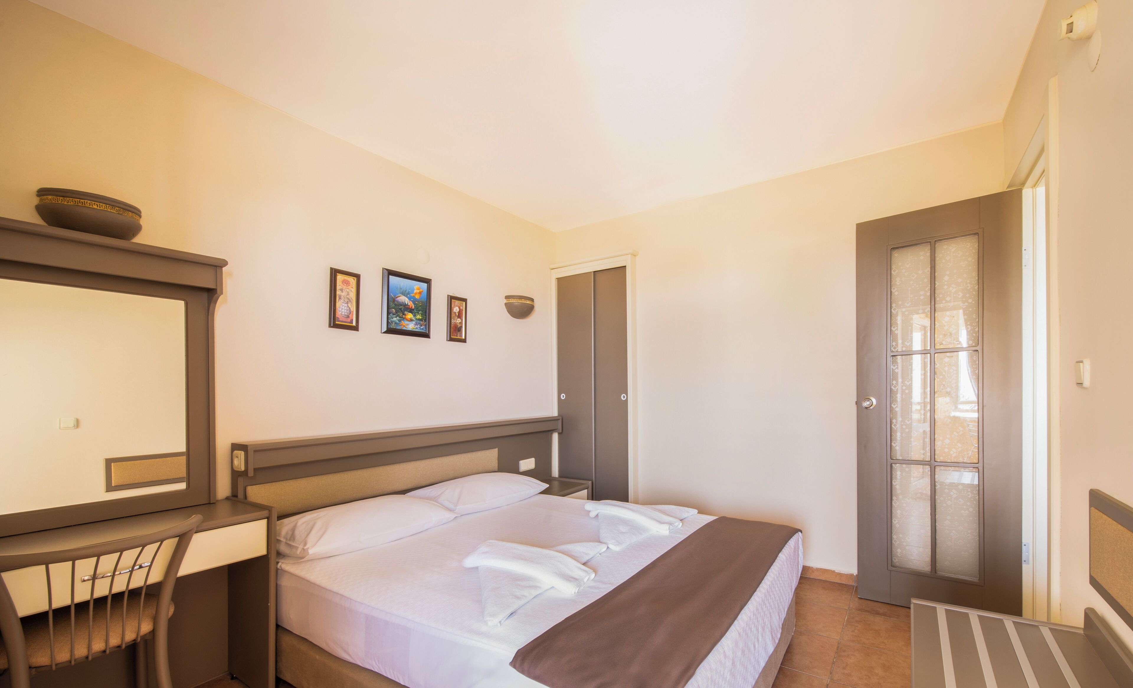 Hotelkamer met een bed, bureau, stoel, kledingkast en een deur met geëtste ruitpanelen.