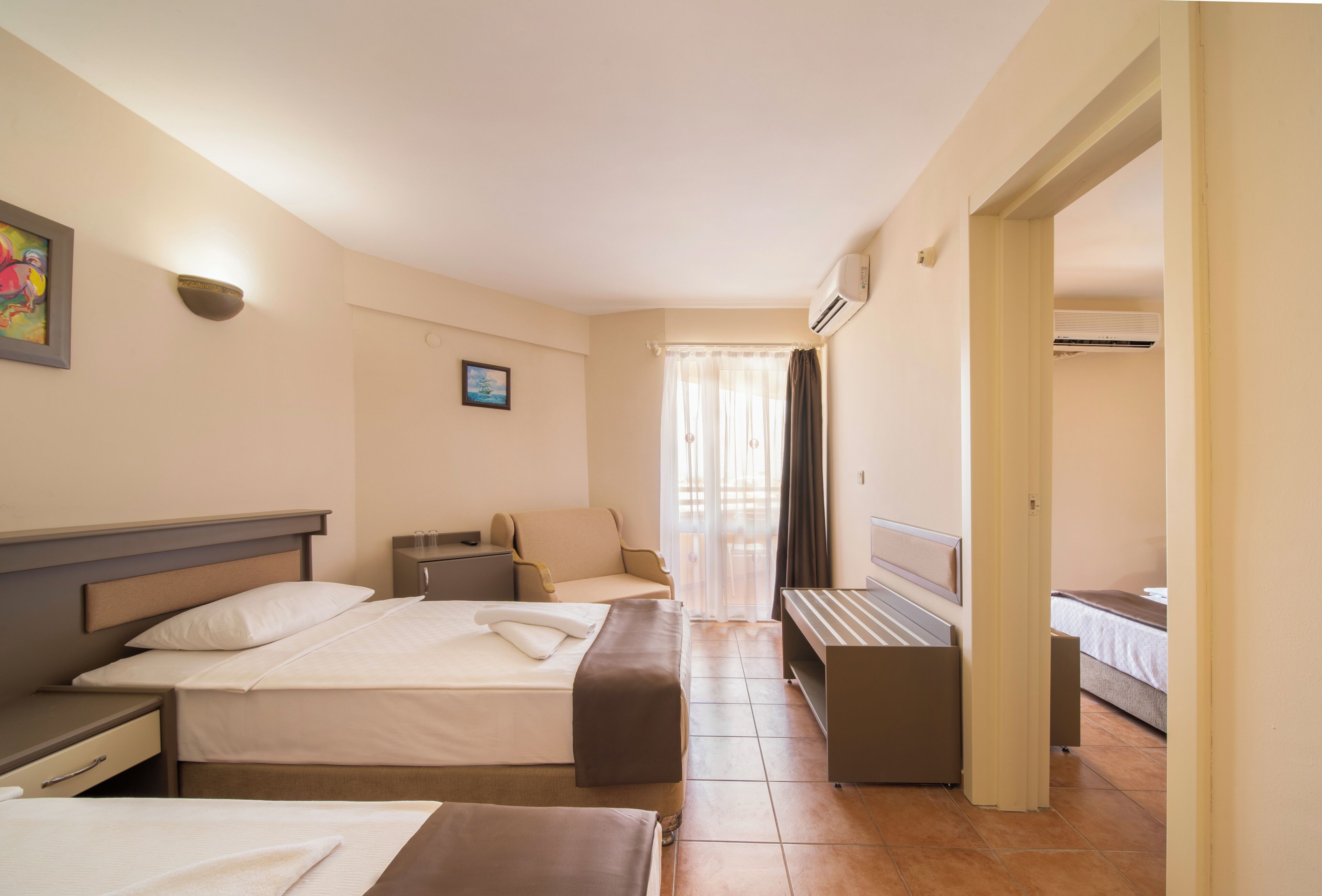 A hotel room with two beds, a sofa, a desk, and a window with curtains.