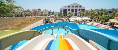 A water slide leading to a pool area with a view of a resort building.