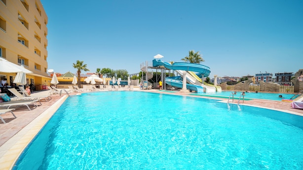 A swimming pool with a water slide, lounge chairs, umbrellas, and a building with balconies. - Hotel Esra Family Suite - All inclusive (Didim)