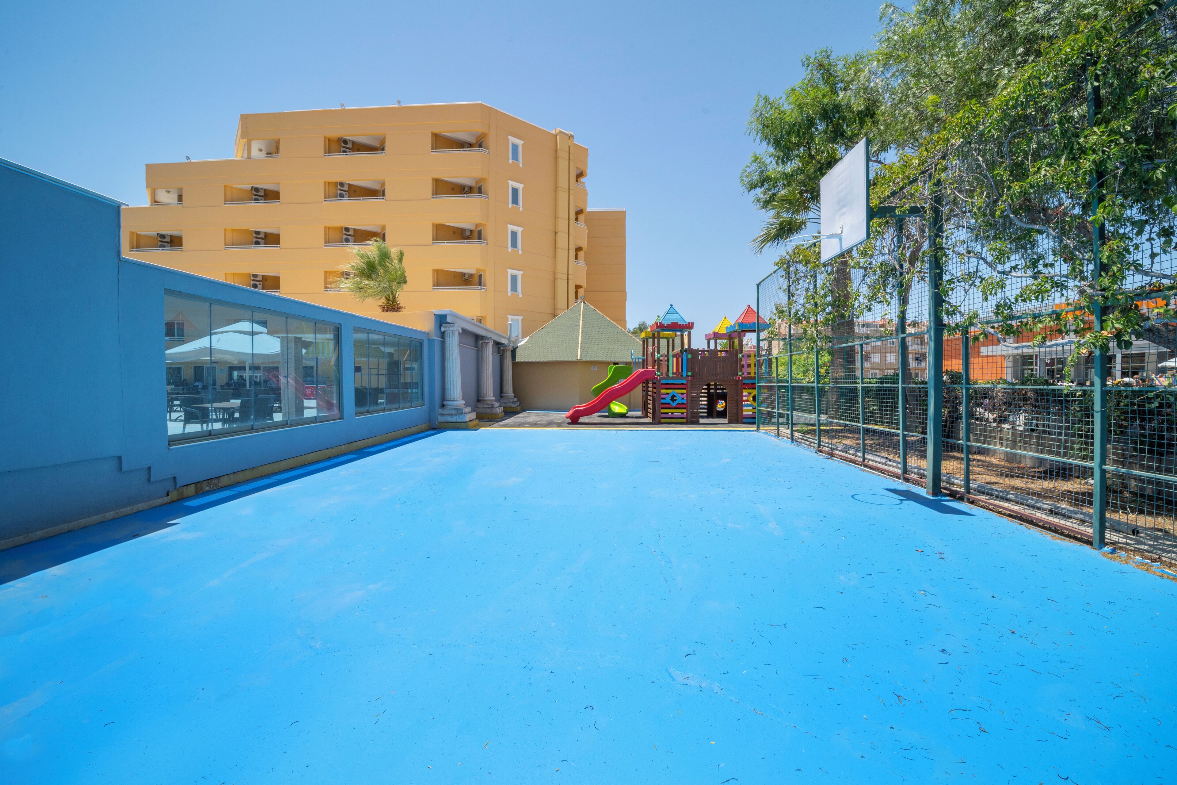 A blue outdoor area with a playground, a building with multiple windows, and a clear sky.