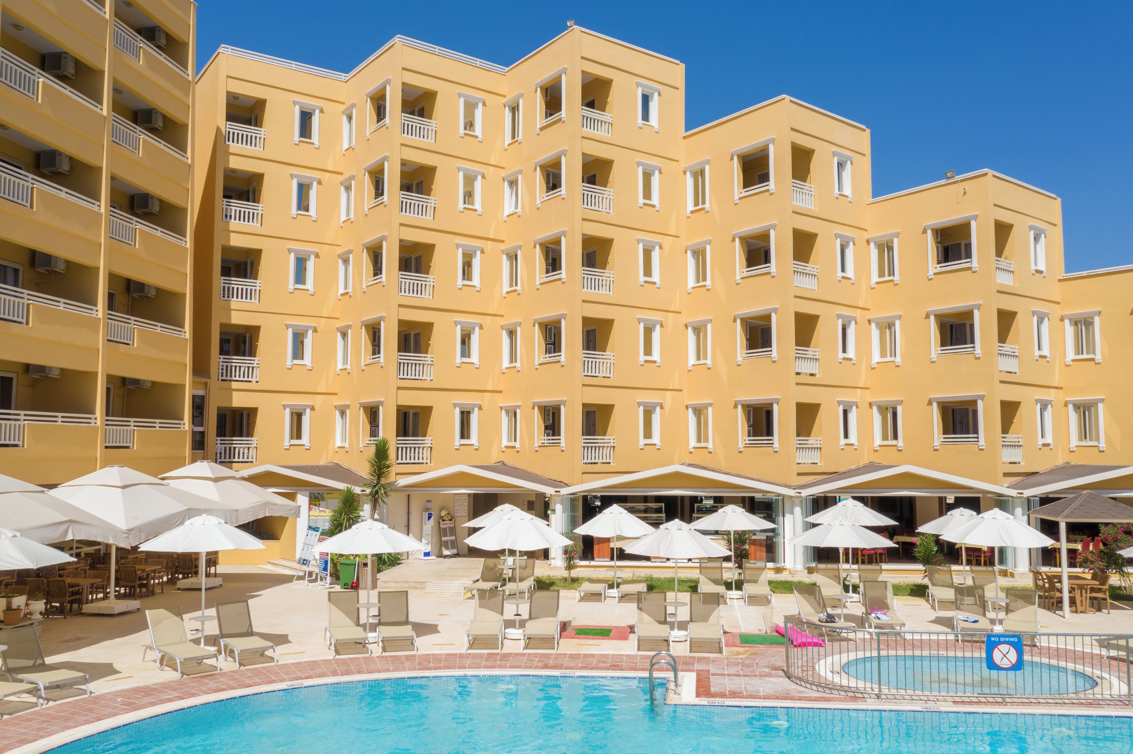 Un hotel con varios balcones, piscina y mobiliario exterior con sombrillas.