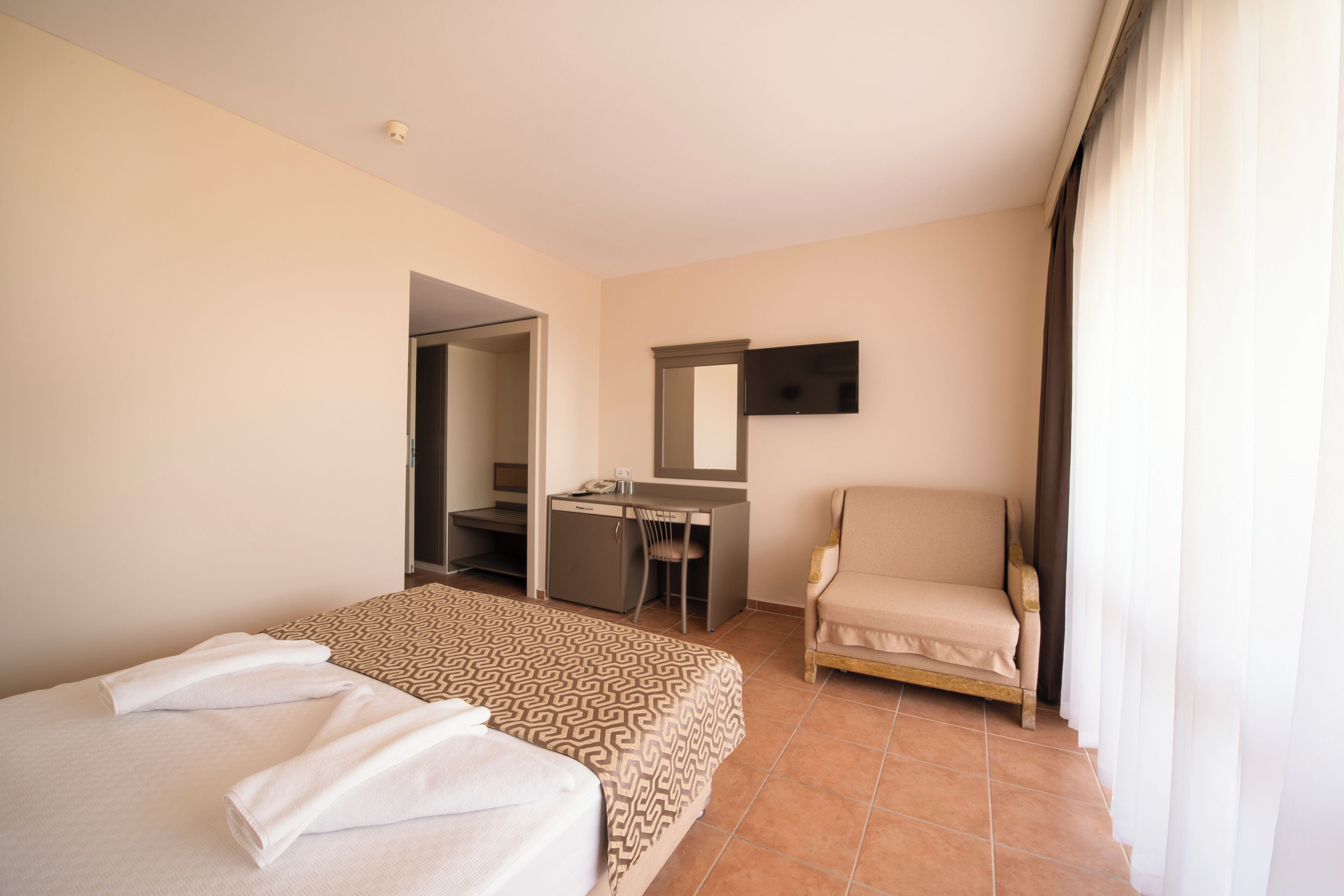 Habitación de hotel con una cama, un escritorio, una silla, un espejo y un televisor.