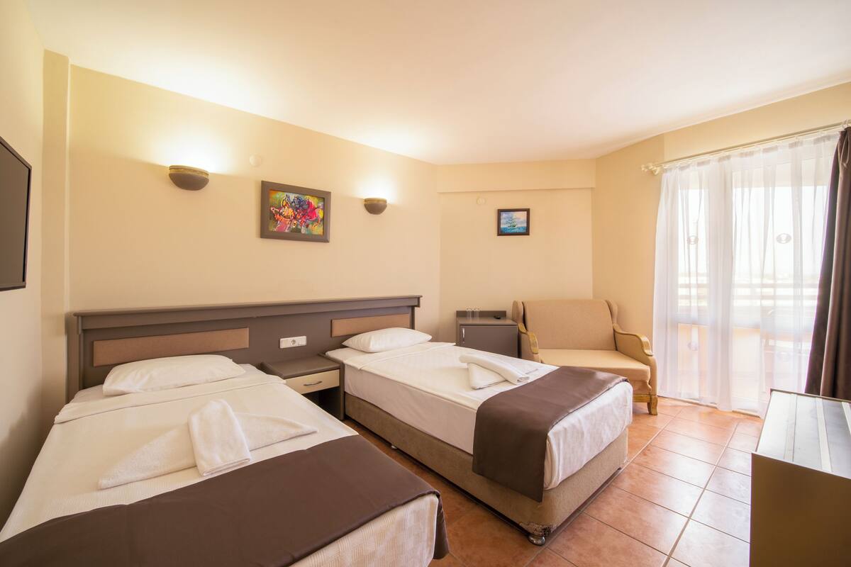 Une chambre d’hôtel avec deux lits, un bureau, une chaise et un balcon avec des rideaux.