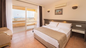 A hotel room with a bed, a nightstand, a chair, a large window with a view, and an air conditioning unit. - Hotel Esra Family Suite - All inclusive (Didim)
