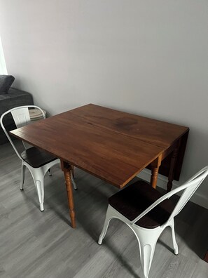 Ein rechteckiger Holztisch mit vier weißen Stühlen, ein graues Sofa und ein grauer Boden.