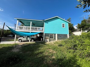 Ein zweistöckiges Haus mit Balkon, davor ein geparkter Lastwagen und eine Hängematte.