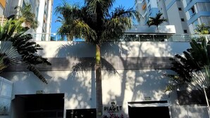 A modern high-rise building with multiple balconies, a palm tree in the foreground, and a scooter parked on the street.