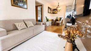 A living room with a sofa, a dining area with a table and chairs, and a decorative vase with dried flowers.