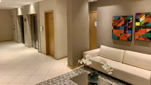 A hotel lobby with a sofa, a coffee table, a vase with flowers, two paintings, and an elevator.